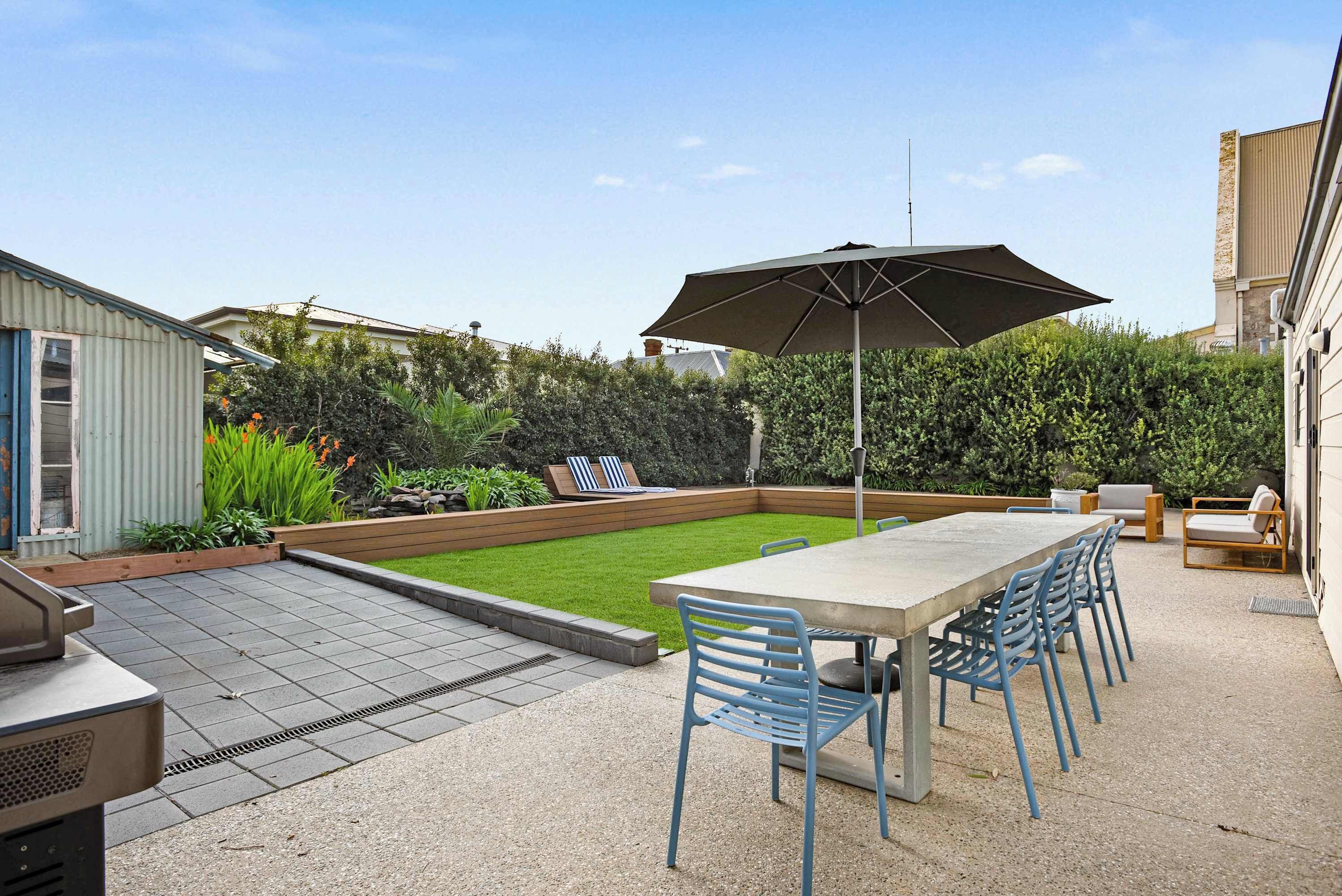 Een terras met een tafel, stoelen, een barbecue en een grote parasol.