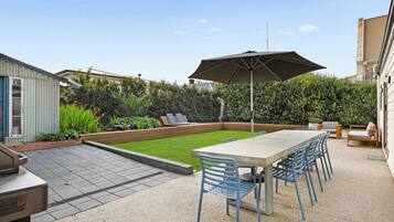 Een terras met een tafel, stoelen, een barbecue en een grote parasol.