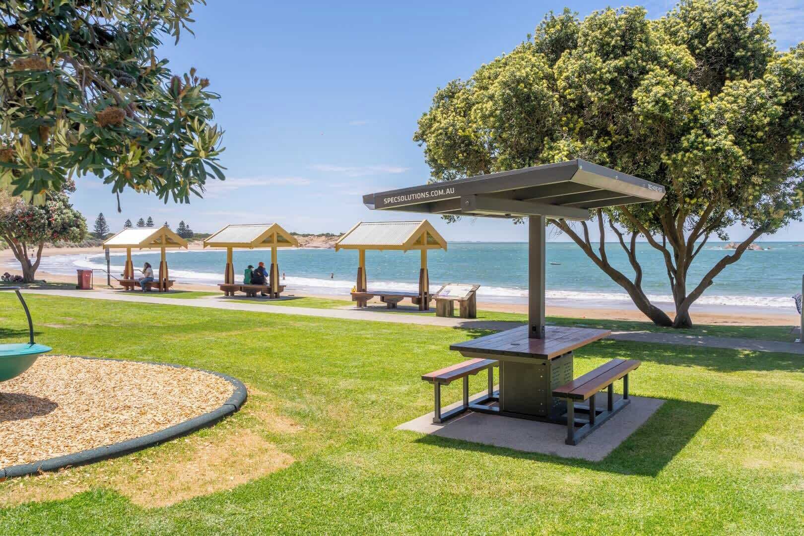 A beachside park with picnic tables, gazebos, and a clear view of the ocean.
