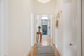 A hallway with a wooden floor, a black and white striped rug, a wooden table with a plant, and a door with a brass handle. - Little Bird Port Elliot | Walk to Beaches & Cafes (Port Elliot)