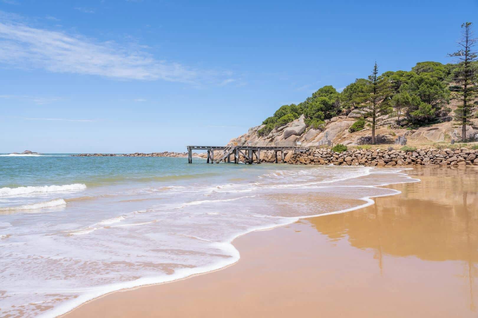 A beach with a rocky cliff, a wooden pier, and clear blue skies.