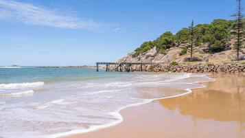 A beach with a rocky cliff, a wooden pier, and clear blue skies.