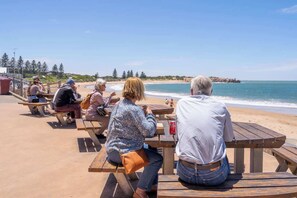 A beachside dining area with wooden tables and benches, overlooking the ocean. - Little Bird Port Elliot, Walk to Beaches & Cafes (Port Elliot)