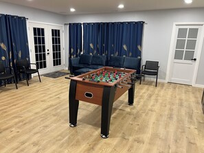 A room with a foosball table, a sofa, and a door. - Harmony home - A Spacious 4-bedroom single family home with AC (Kirkland)