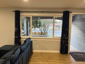 A room with a large window, a black sofa, and a wooden floor. - Harmony home - A Spacious 4-bedroom single family home with AC (Kirkland)
