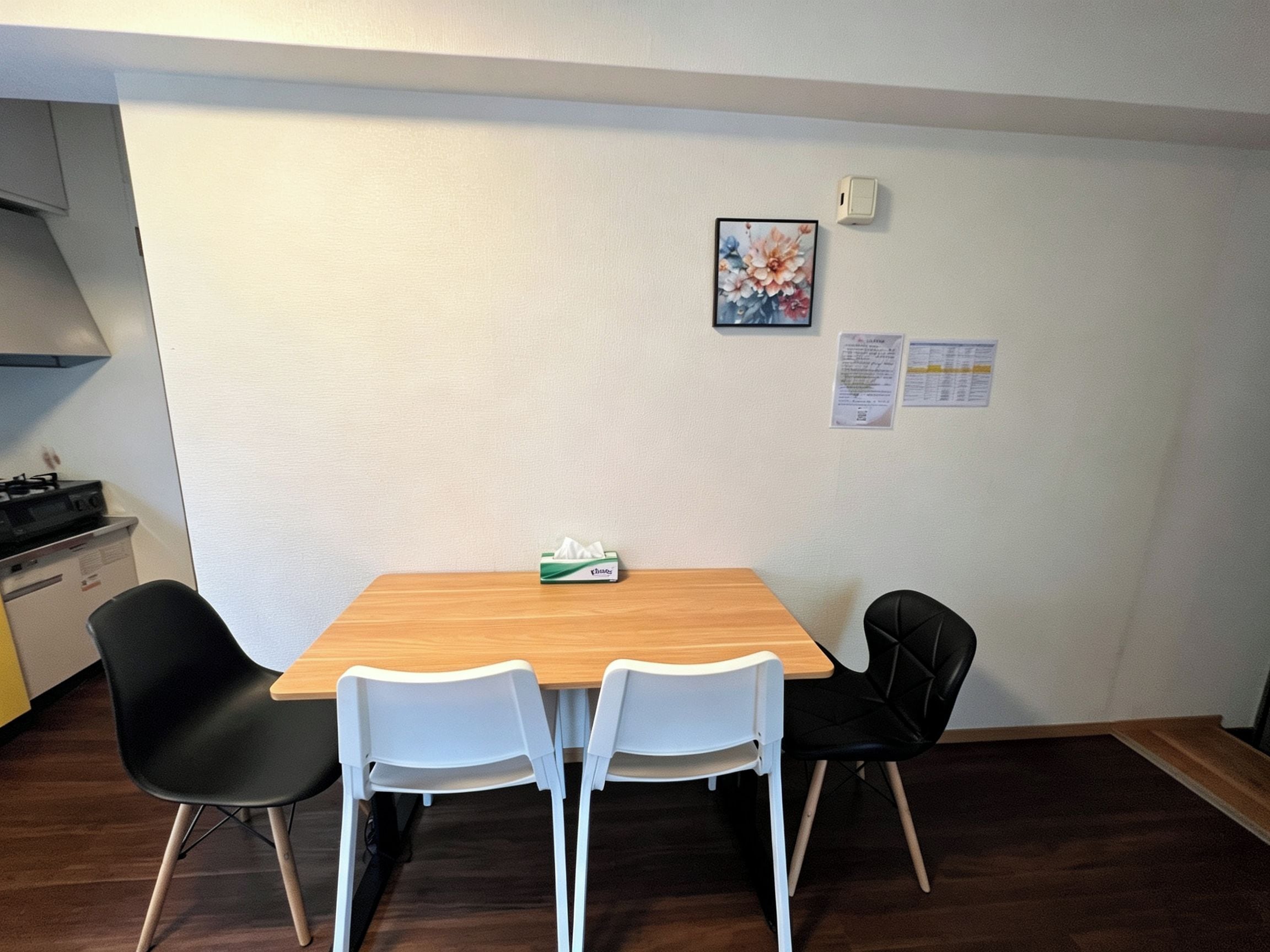 A dining area with a wooden table, two white chairs, and a black chair. There is a box of tissues on the table.