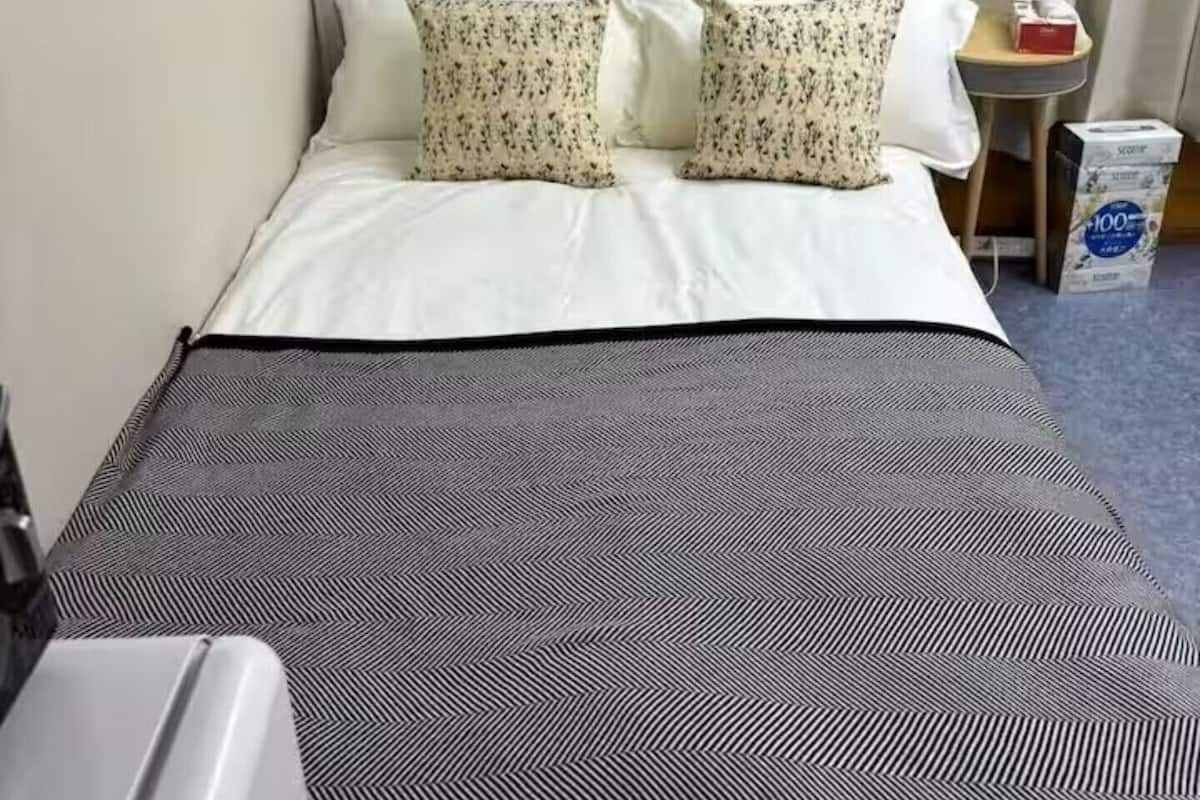 Una habitación de hotel con cama, almohadas, una mesita y un cubo de basura.