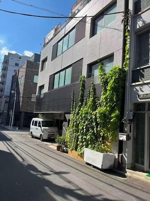 Un edificio moderno con una camioneta blanca estacionada frente, cielo despejado y una calle con sombras.