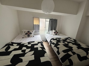 A bedroom with two beds, a window with curtains, and a hanging light fixture.