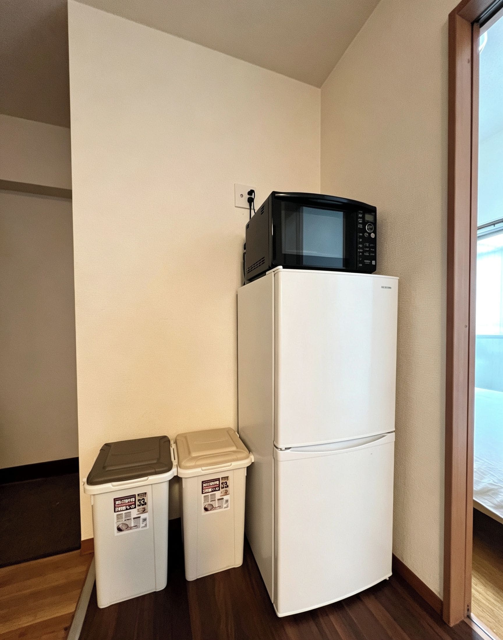 A compact kitchen with a white refrigerator and a microwave on top. There are two storage bins against the wall.