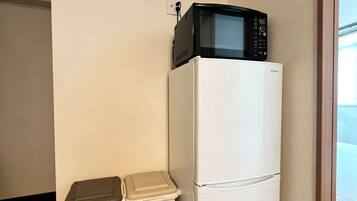 A compact kitchen with a white refrigerator and a microwave on top. There are two storage bins against the wall.