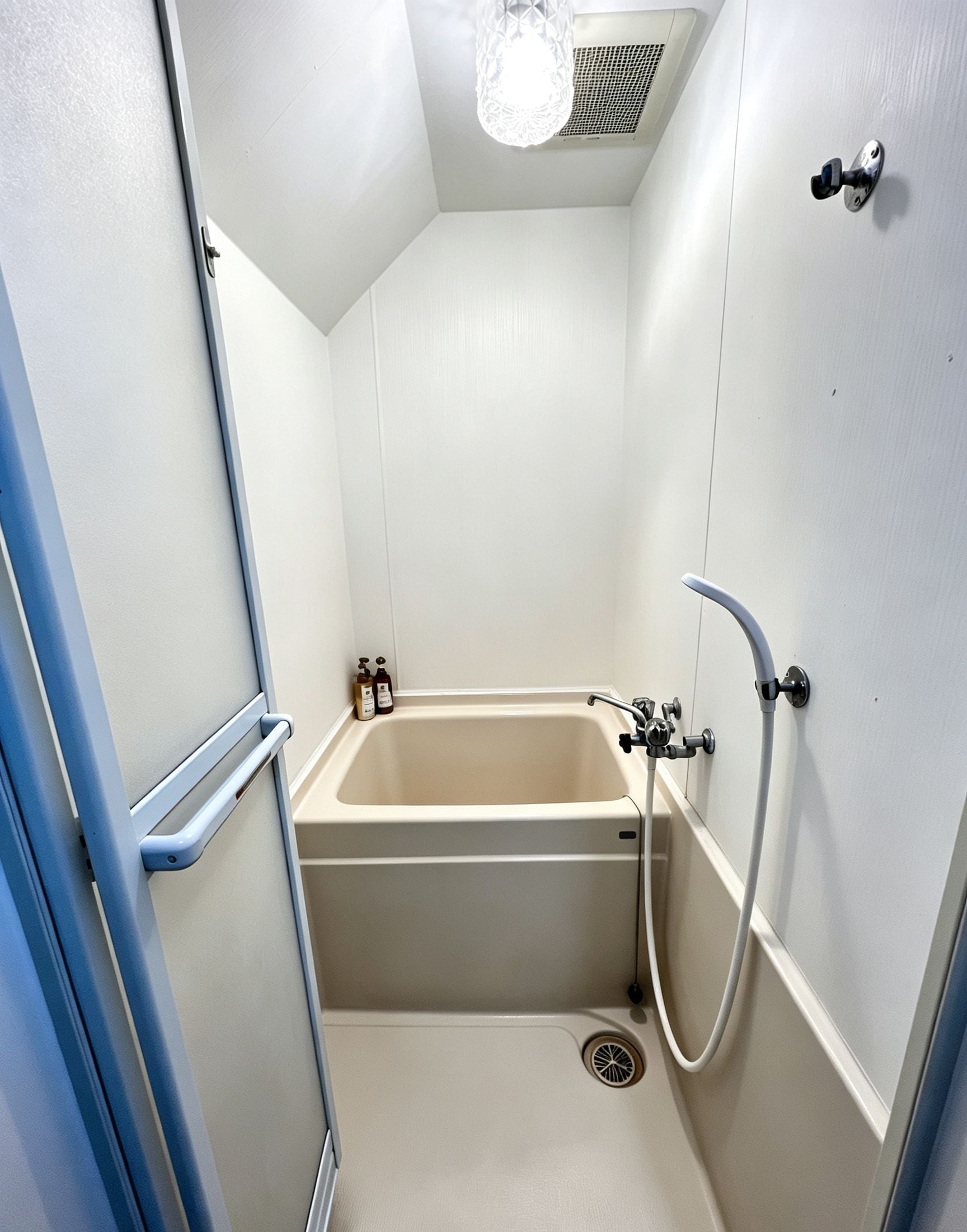 Un petit espace douche fermé, équipé d’une baignoire, d’une douchette à main et d’un robinet mural.