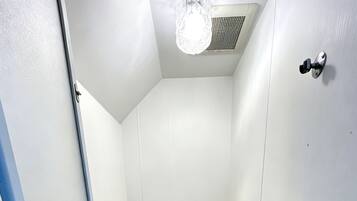 Un petit espace douche fermé, équipé d’une baignoire, d’une douchette à main et d’un robinet mural.