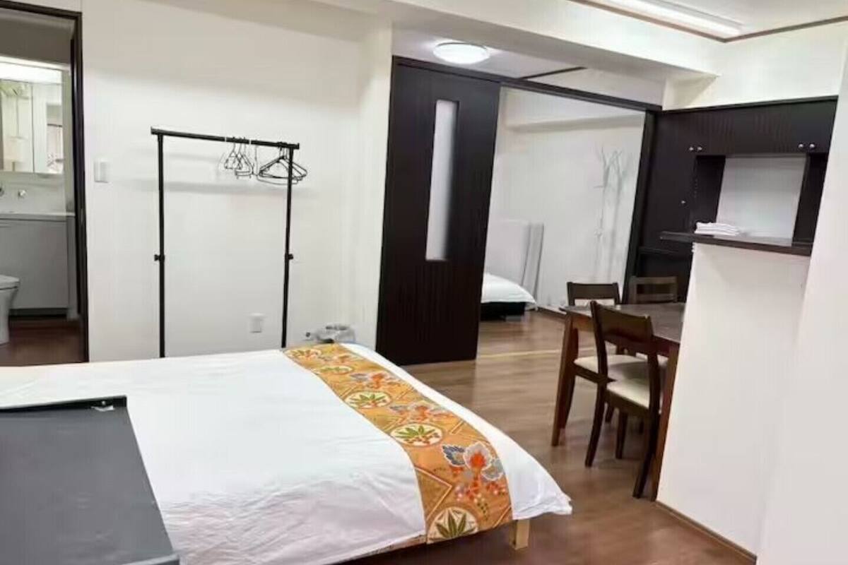 Habitación de hotel con cama, escritorio, silla, armario y baño visible a través de una puerta abierta.