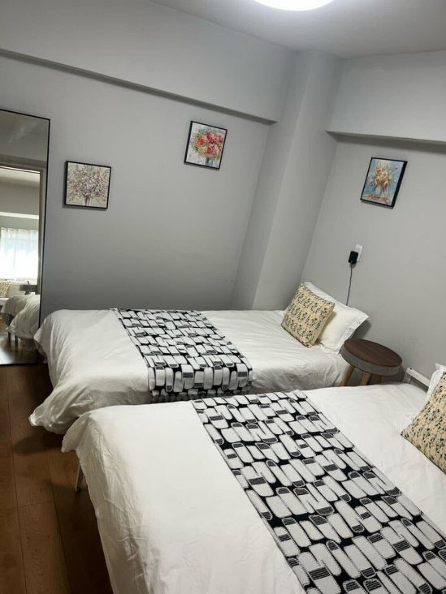 Une chambre avec deux lits, une table d’appoint ronde en bois et deux tableaux représentant des motifs floraux, encadrés et accrochés aux murs.