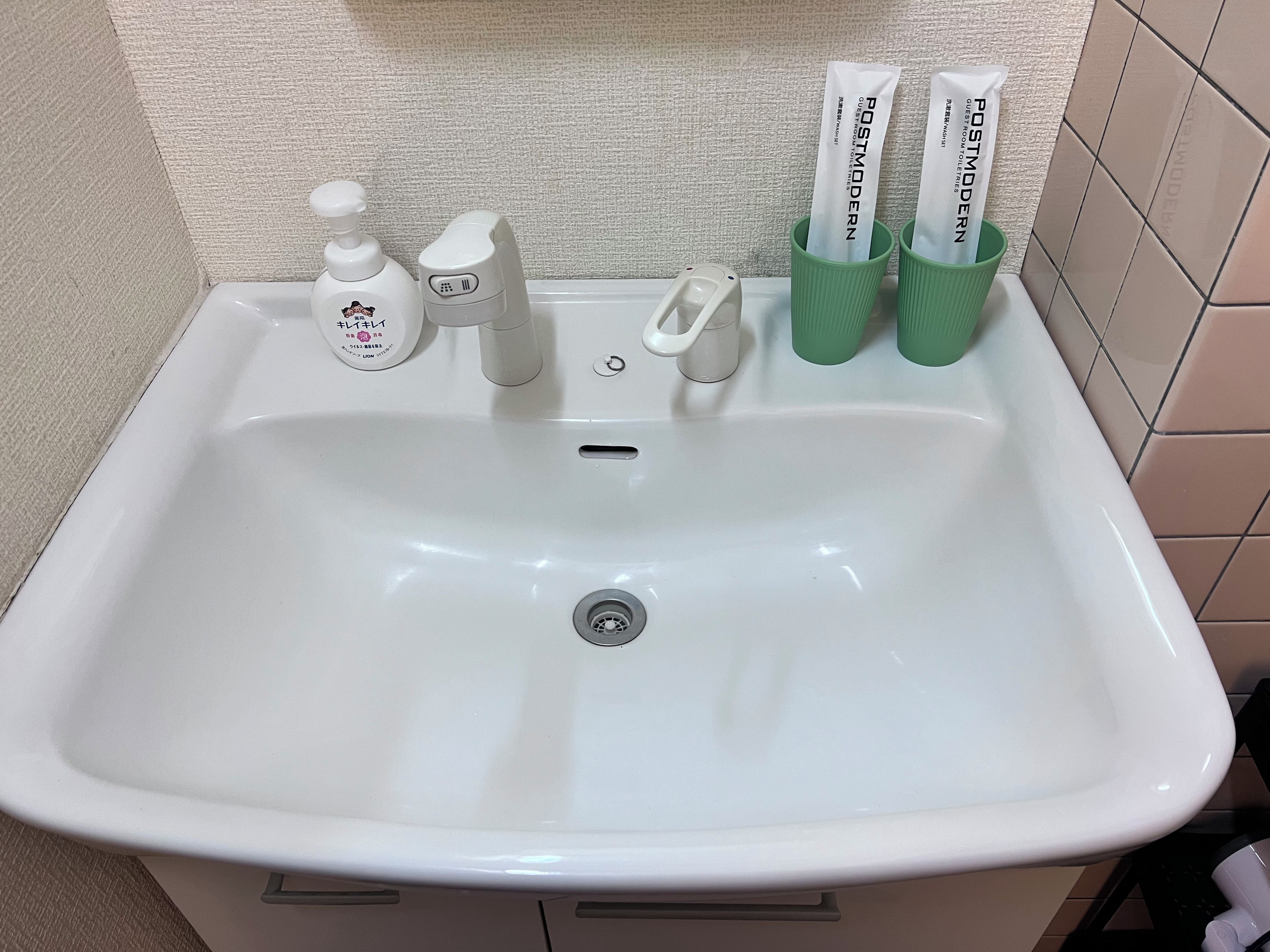A white bathroom sink with a soap dispenser, a faucet, and two green toothbrush holders with toothpaste.