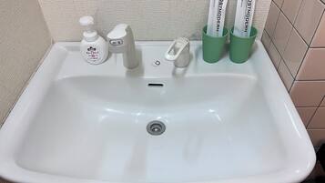 A white bathroom sink with a soap dispenser, a faucet, and two green toothbrush holders with toothpaste.