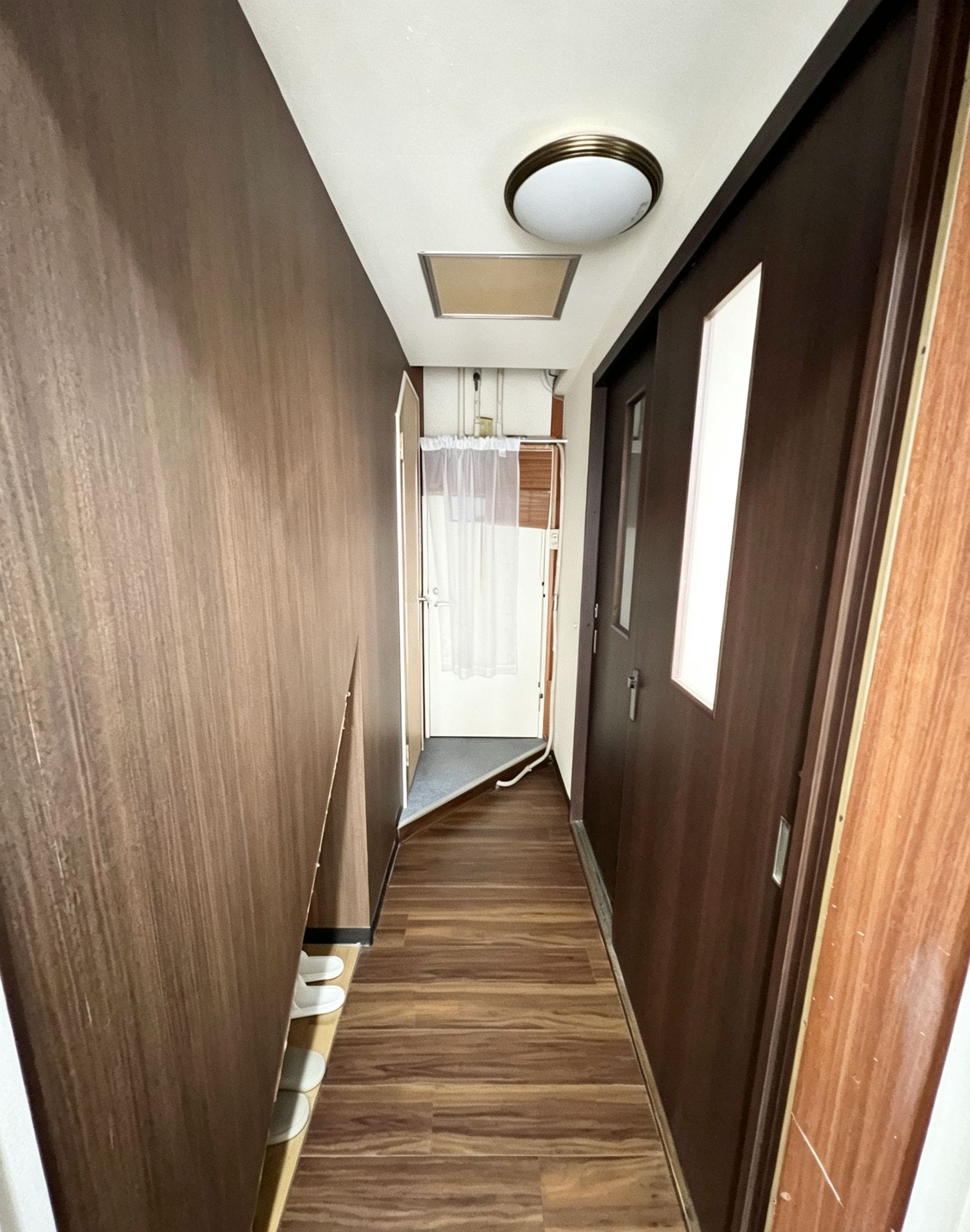 Un estrecho pasillo con paredes y piso de madera, que conduce a una habitación con ventana y puerta.