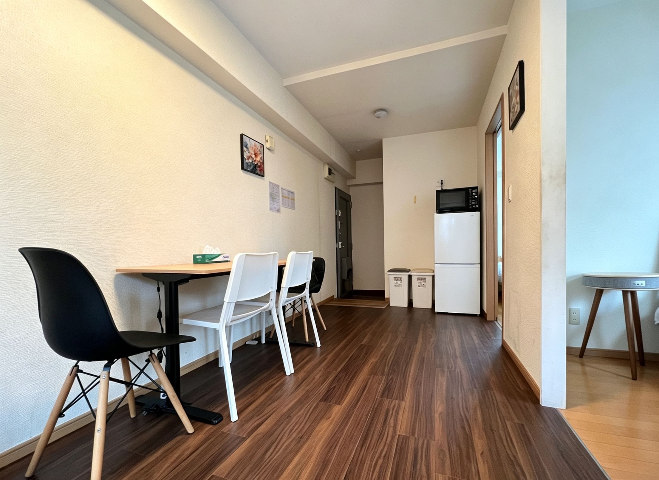 A compact kitchen with a microwave and refrigerator, a dining area with chairs and a table, and a hallway with a door leading to another room.