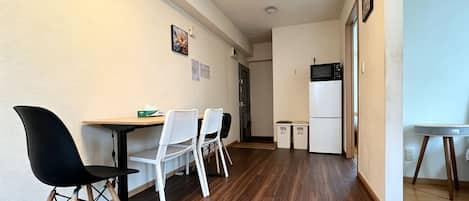 Een compacte keuken met een magnetron en koelkast, een eethoek met stoelen en een tafel, en een gang met een deur naar een andere kamer.