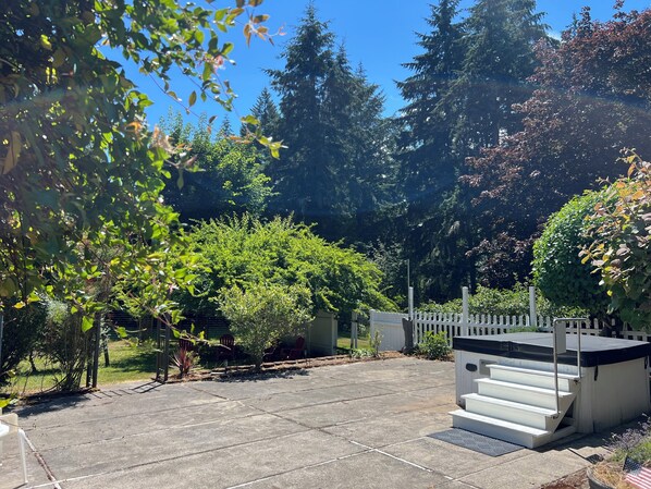 A patio area with a white fence, a covered outdoor seating area, and various trees and shrubs.