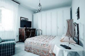 Una camera da letto con un letto, una TV, un armadio, una cassettiera, una sedia e una lampada.