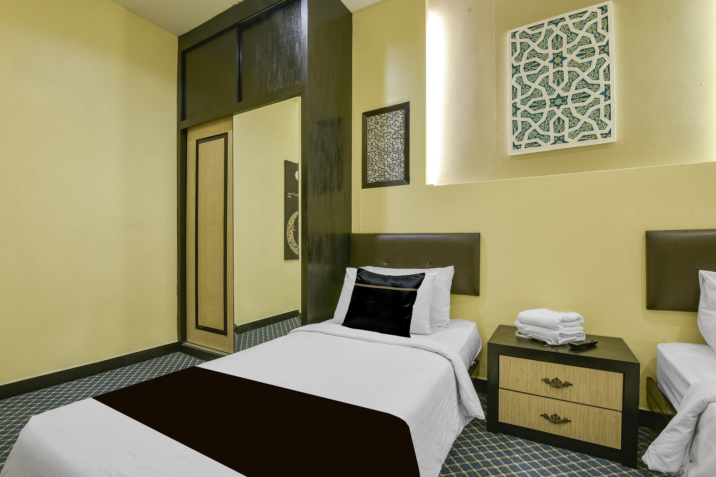 A hotel room with a bed, bedside tables, a wardrobe, and decorative wall art.
