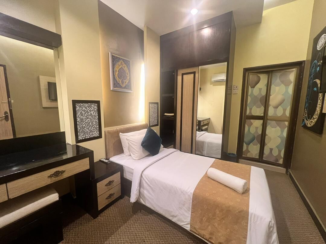 Quarto de hotel com cama, mesa de cabeceira, cômoda e um espelho grande.
