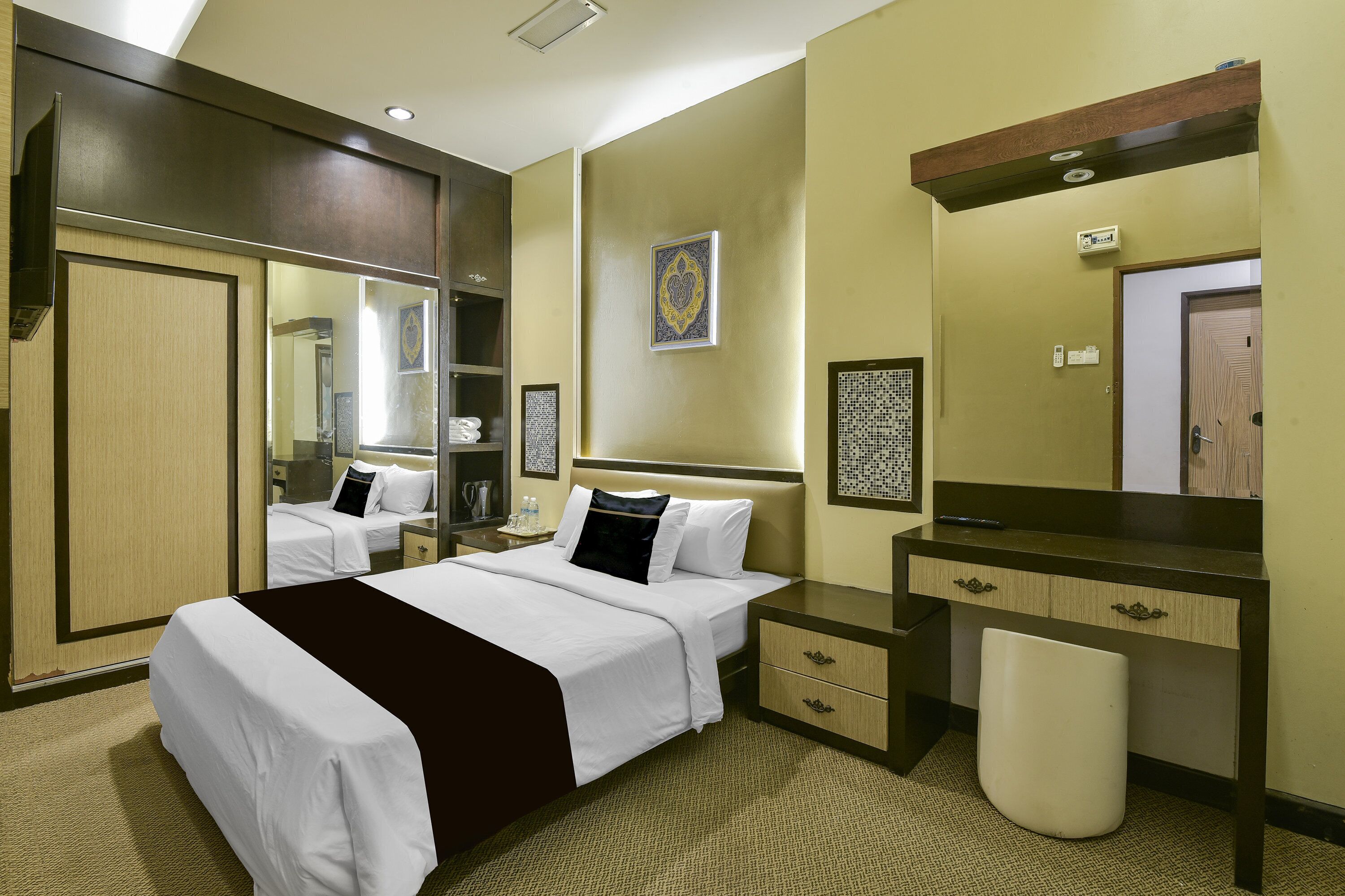 A hotel room with a bed, bedside tables, a mirror, a desk, and a trash bin.