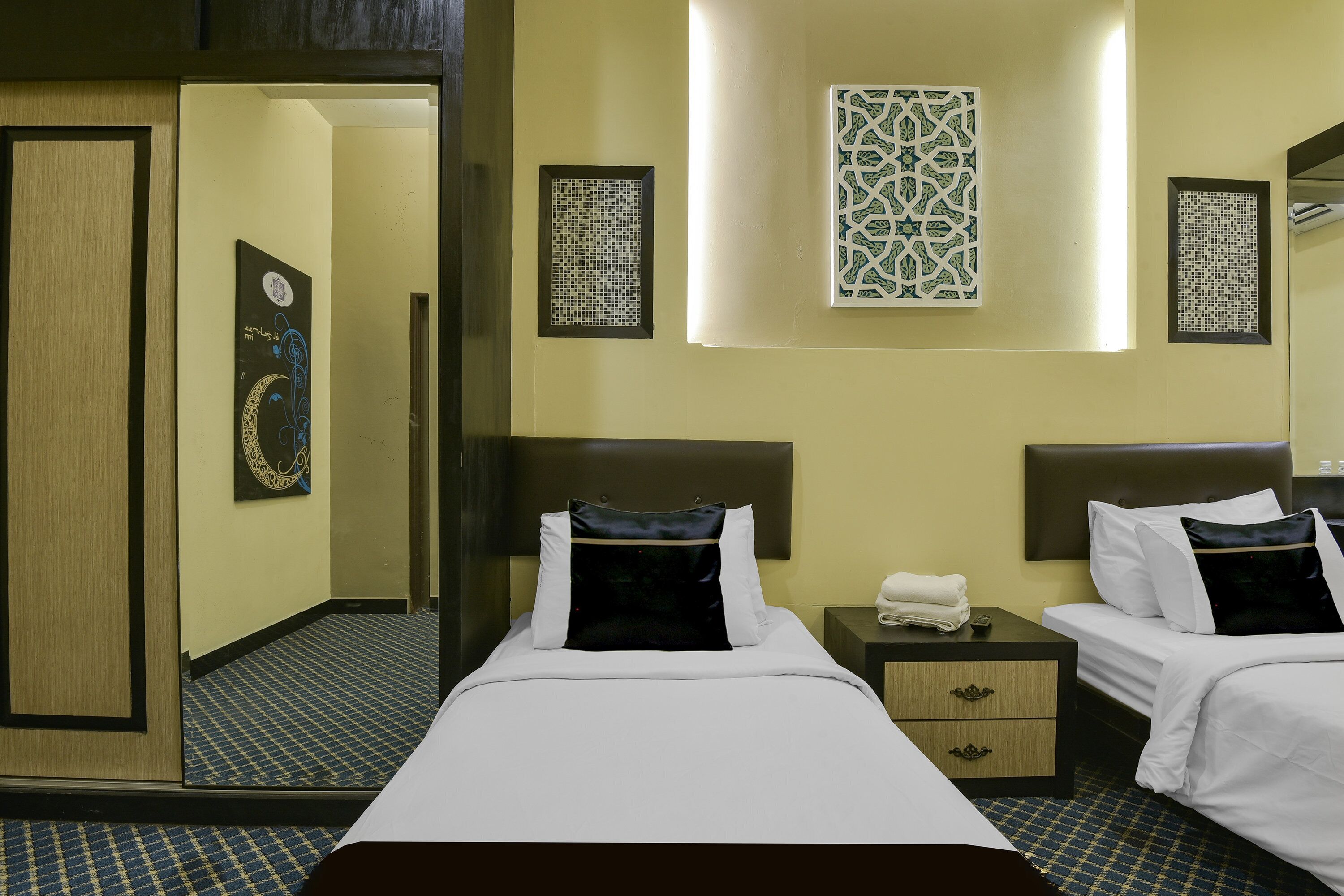 A hotel room with two beds, a nightstand, a mirror, and decorative wall art.
