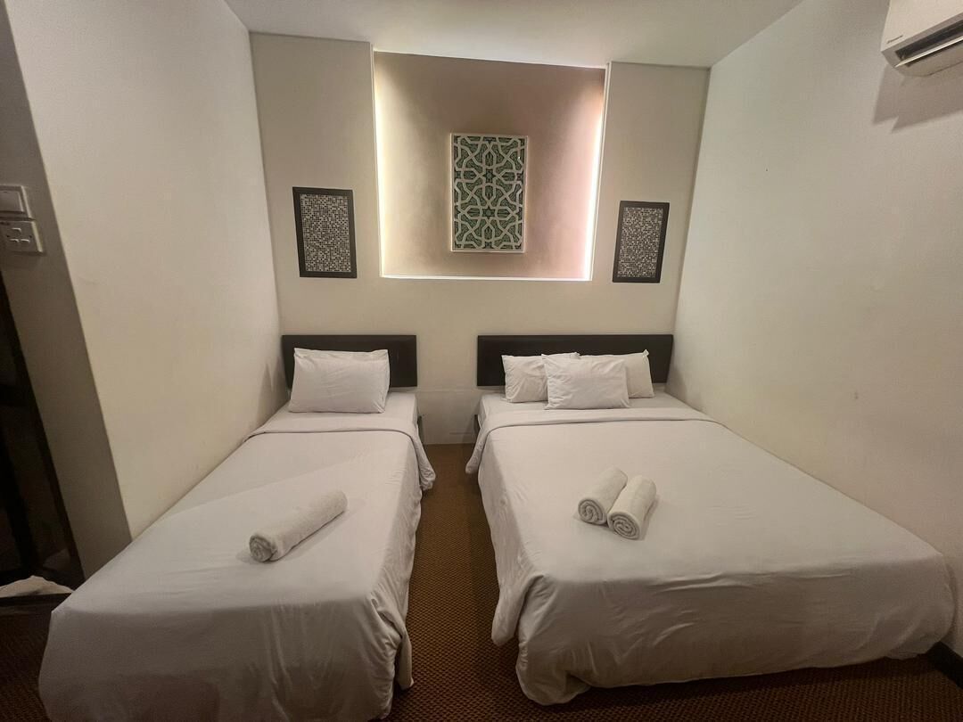 Quarto de hotel com duas camas de solteiro, uma janela pequena com iluminação decorativa e obras de arte nas paredes.