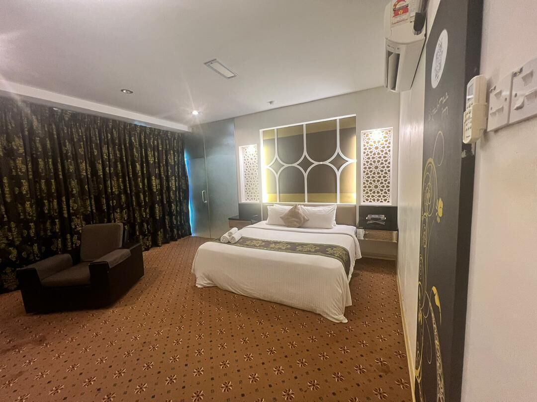 Quarto de hotel com uma cama grande, um sofá, um tapete estampado e painéis decorativos na parede.