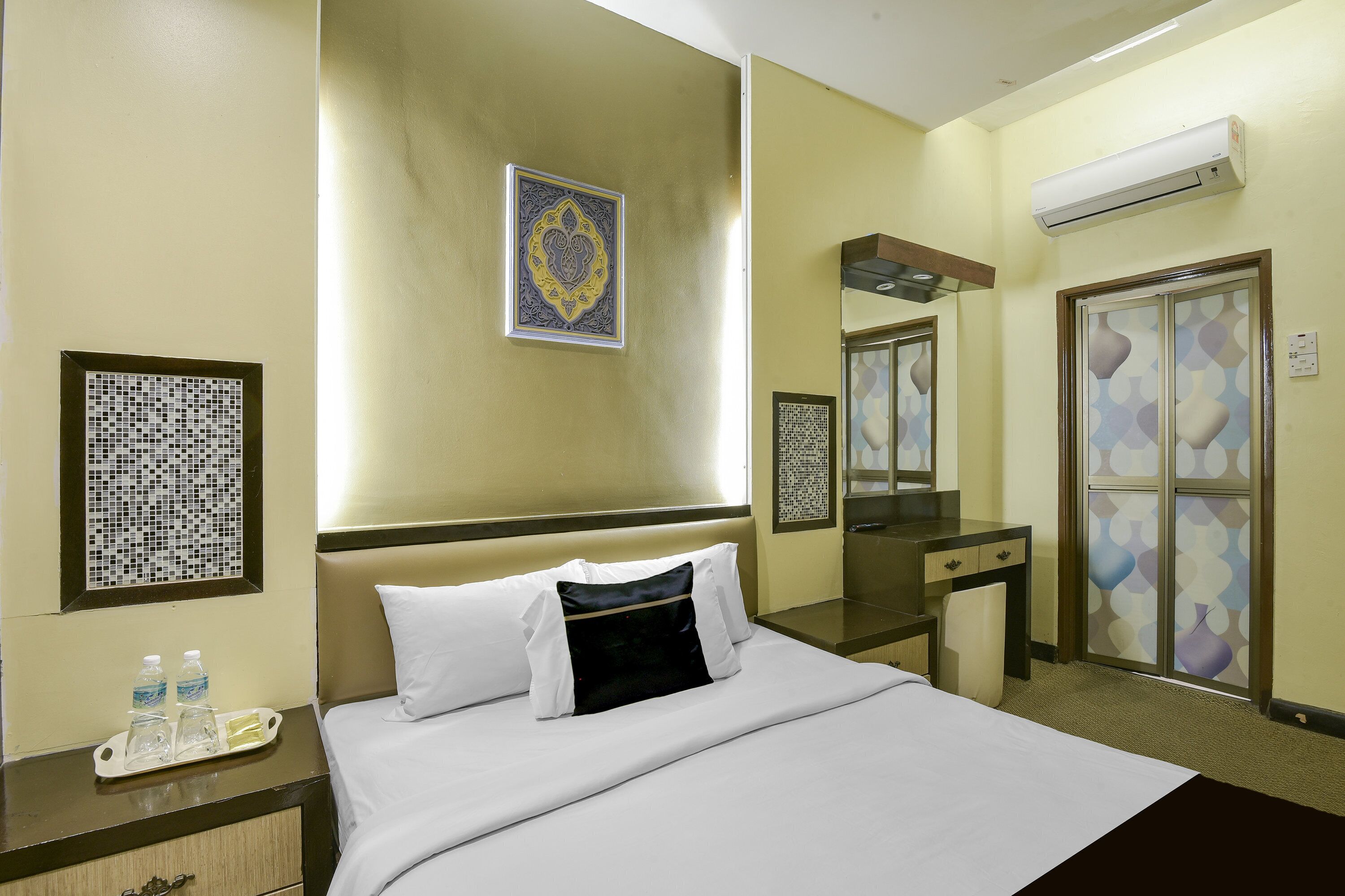Habitación de hotel con cama, escritorio, espejo, aire acondicionado y una obra de arte colgada en la pared.