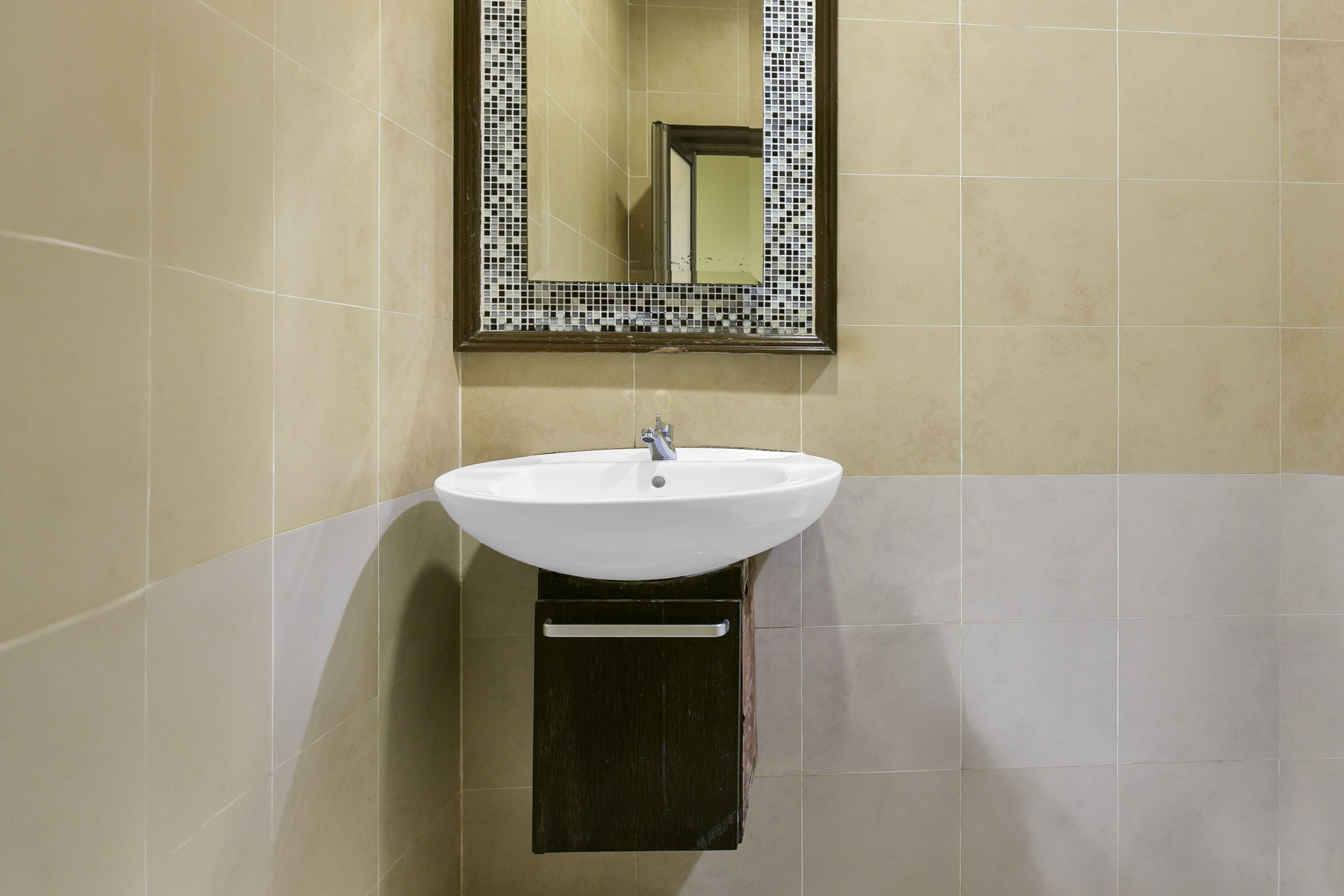 Un baño con lavabo blanco, espejo con marco de mosaico y paredes de azulejos.