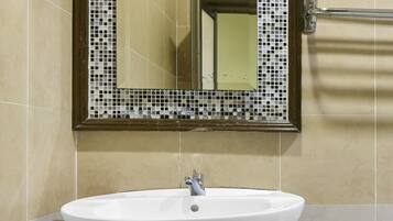 A bathroom with a white sink, a mirror with a mosaic border, and a toilet.
