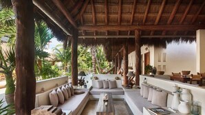 A spacious outdoor lounge area with thatched roof, wooden pillars, and comfortable seating. - Tierra del Mar (Isla Holbox)