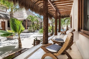 A covered outdoor seating area with wooden lounge chairs and a thatched roof structure.