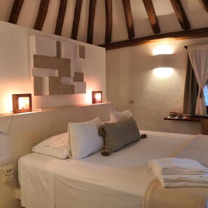 A hotel room with a bed, pillows, a wall-mounted light, a bedside table with a lamp, and a window with curtains. - Tierra del Mar (Isla Holbox)