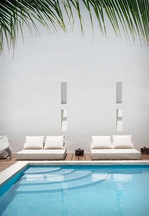 A poolside area with two white lounge chairs, a small table, and a wall with two rectangular light fixtures. - Tierra del Mar (Isla Holbox)