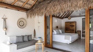 A room with a thatched roof, a bed, a sofa, and a small table. - Tierra del Mar (Isla Holbox)