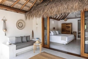 Ein Zimmer mit Strohdach, einem Bett, einem Schlafsofa und einem kleinen Tisch.