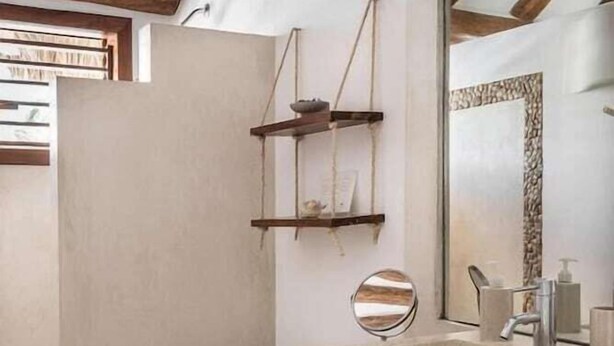Un baño moderno con lavamanos de piedra, vigas de madera, un espejo y un inodoro.