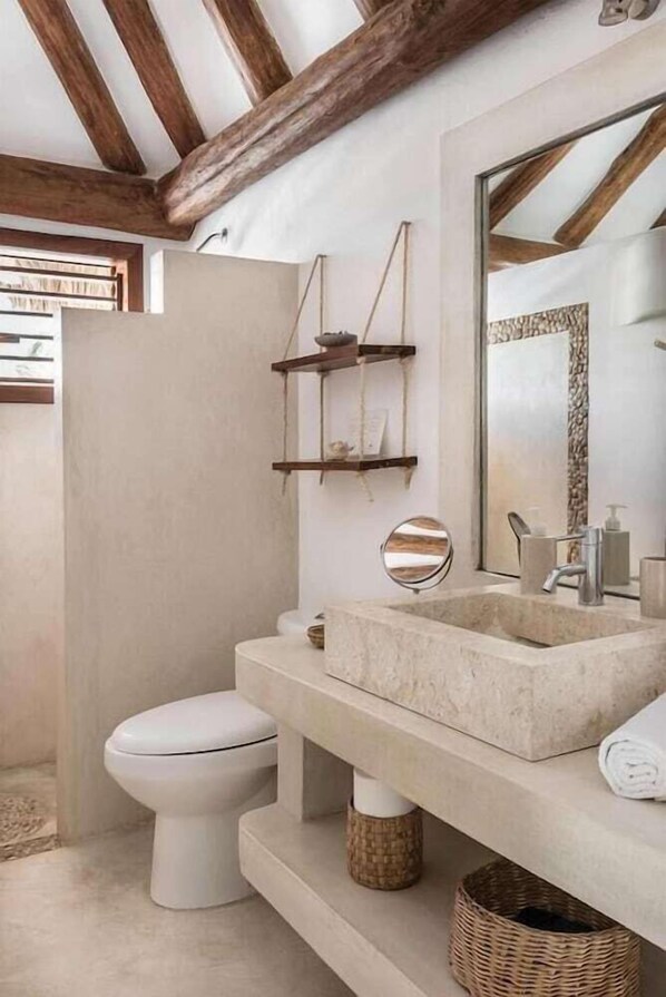 A modern bathroom with a stone sink, wooden beams, a mirror, and a toilet. - Tierra del Mar (Isla Holbox)