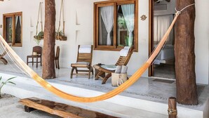 Una hamaca, sillas de madera, una mesita y una ventana con cortinas.
