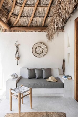 A minimalist living room with a sofa, a woven chair, a decorative wall hanging, and a thatched ceiling. - Tierra del Mar (Isla Holbox)