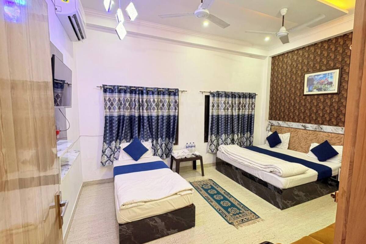 A hotel room with two beds, a small table, a rug, and a ceiling fan.