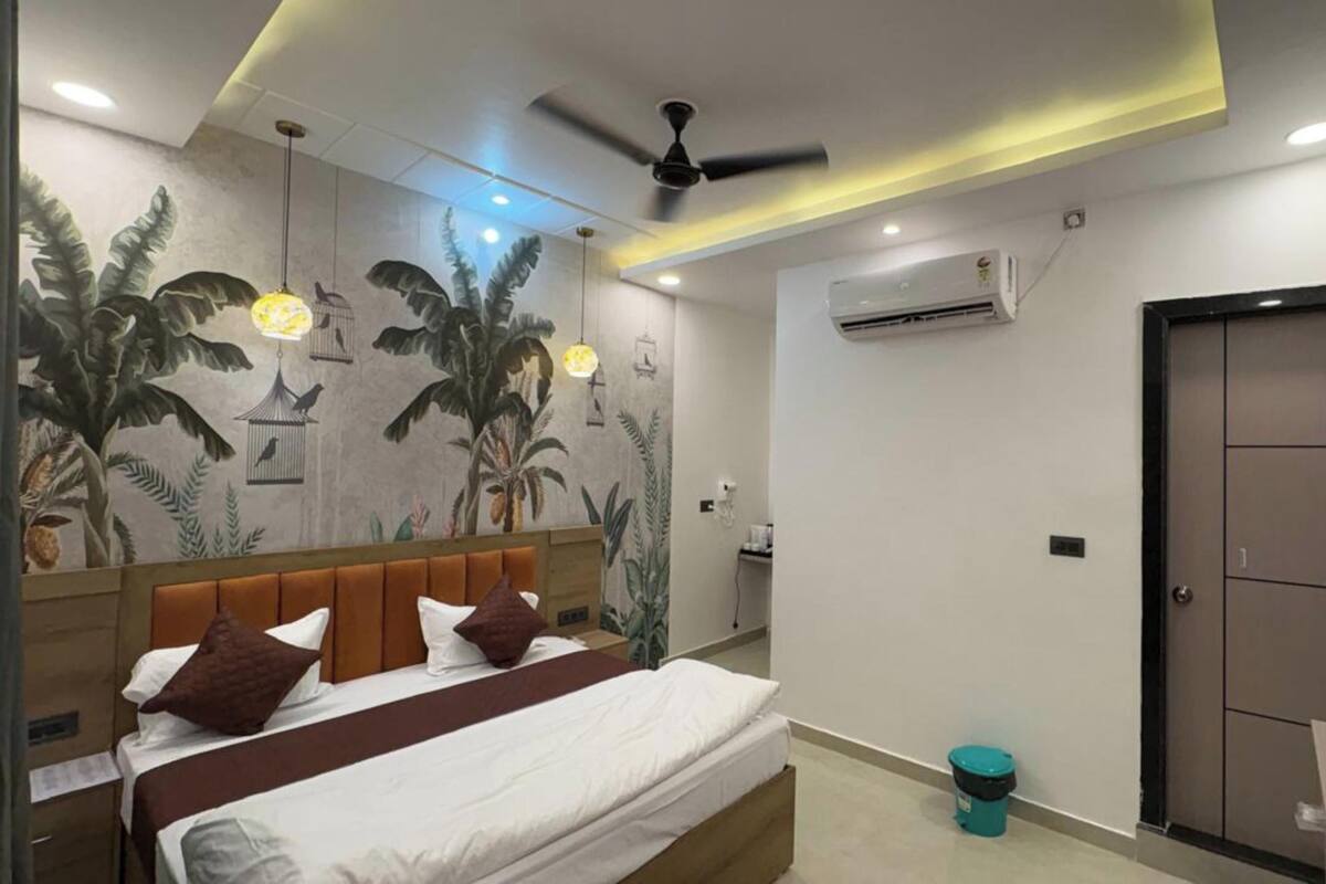 A bedroom with a bed, a ceiling fan, an air conditioning unit, a television, and a door.