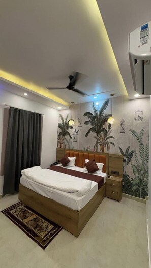Un dormitorio con cama, ventilador de techo, mesita de noche, aire acondicionado instalado en la pared y un mural de plantas tropicales.