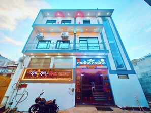 Un edificio de dos pisos con un letrero que dice 'Radhe Radhe Guest House' y un letrero de neón que dice 'Radhai Radhe'.