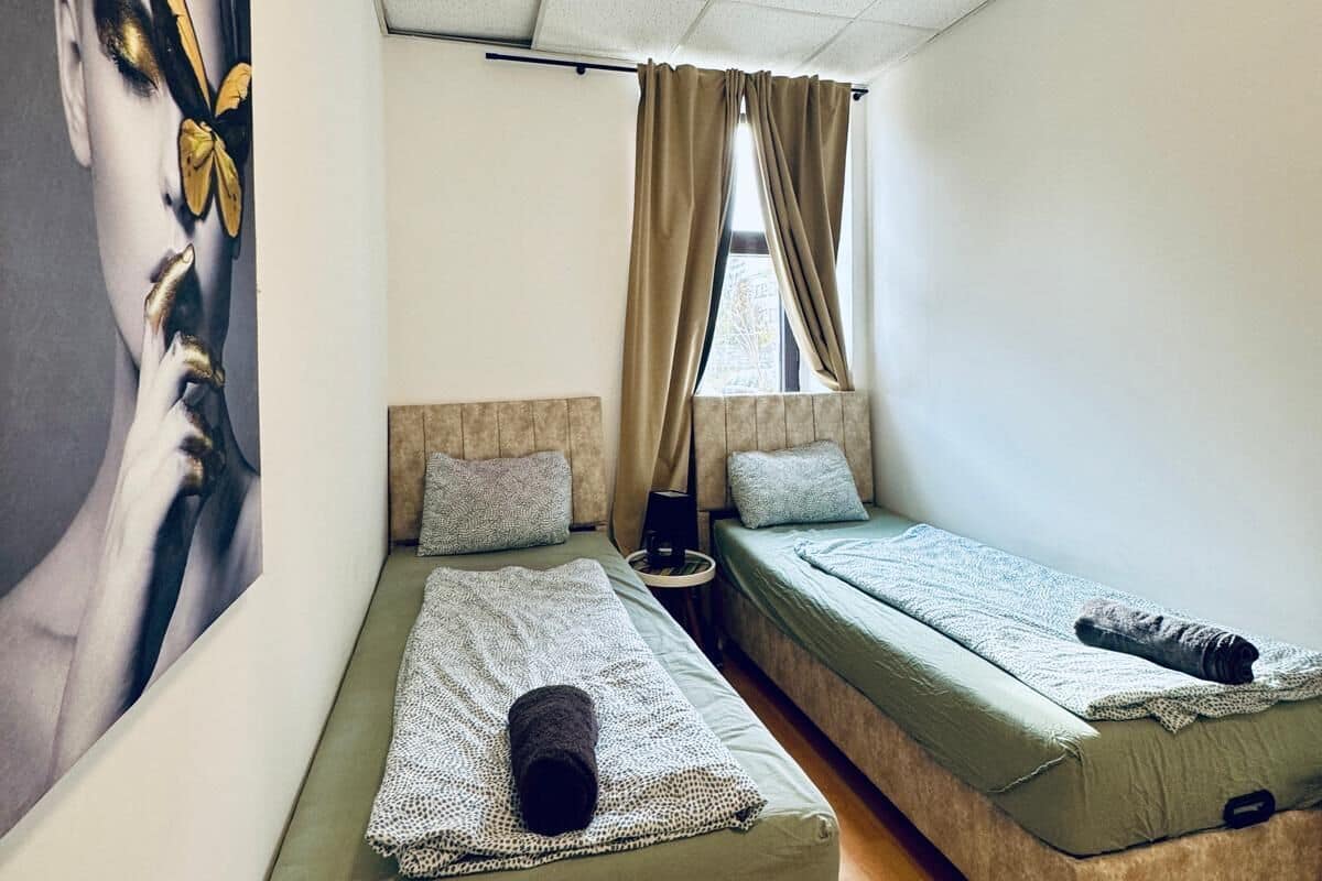 Une chambre avec deux lits, un grand tableau au mur et une fenêtre avec des rideaux.